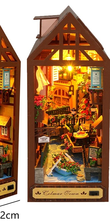 The Colmar Town book nook glowing on a shelf between books
